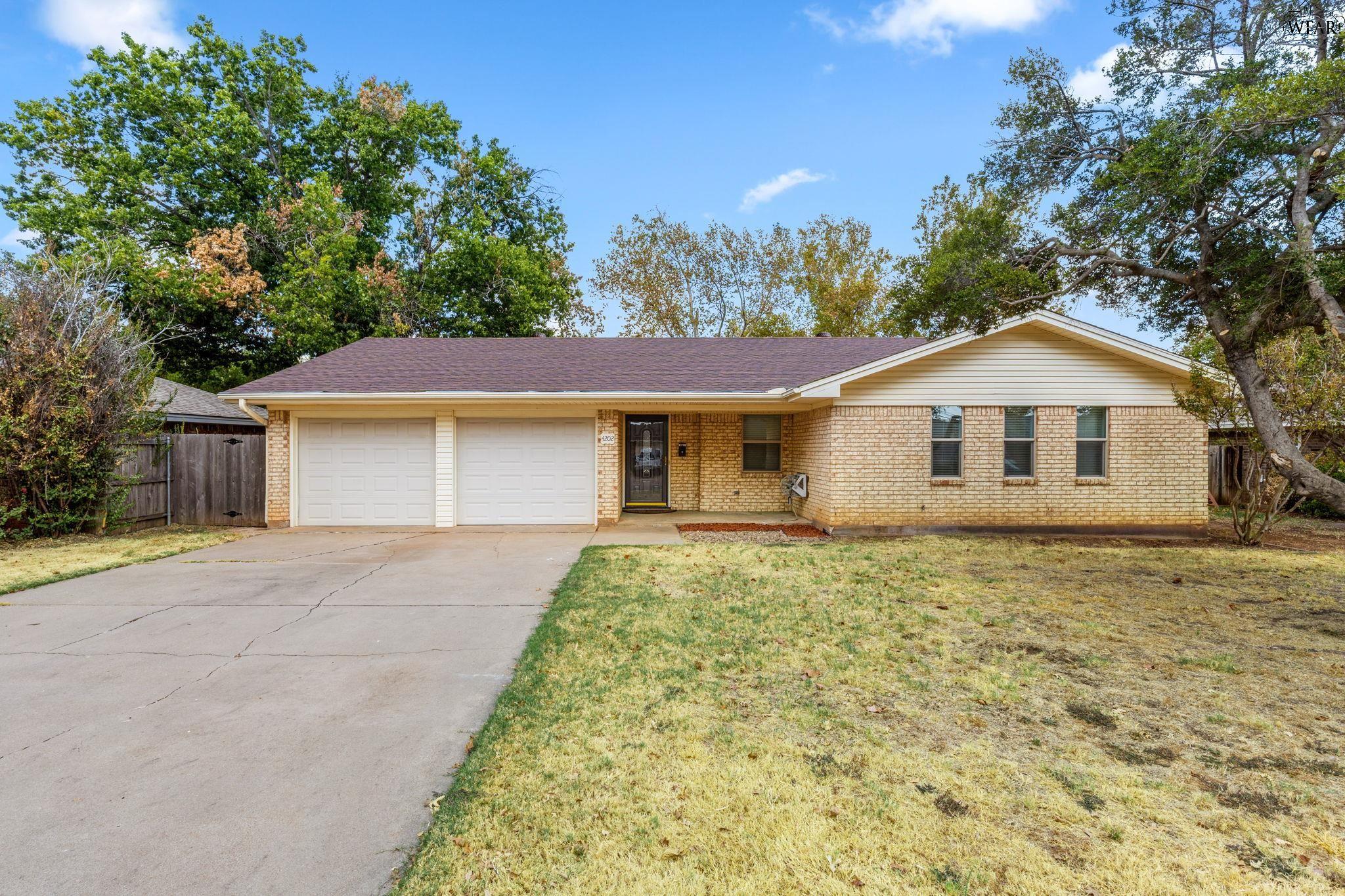 Single-story brick home with a two-car garage, wide driveway, and mature trees.