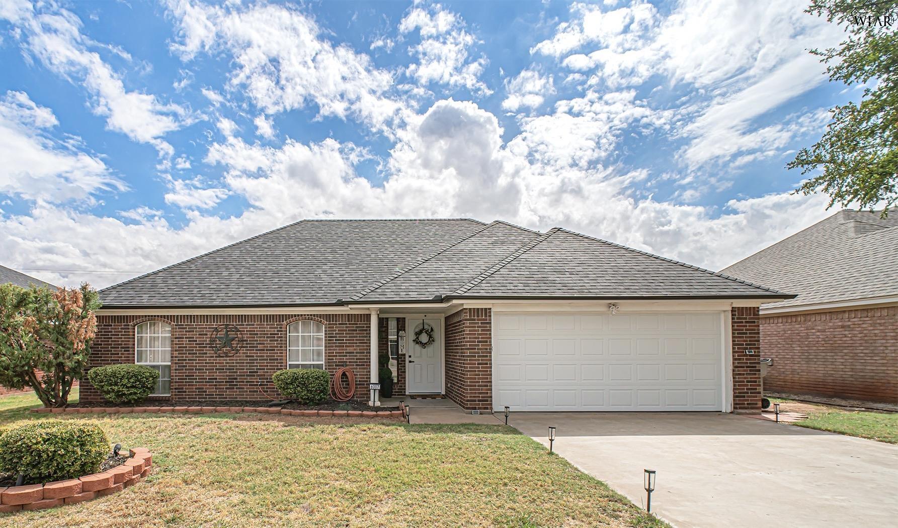 Single-story brick home with a gray hipped roof, white garage, and front lawn.