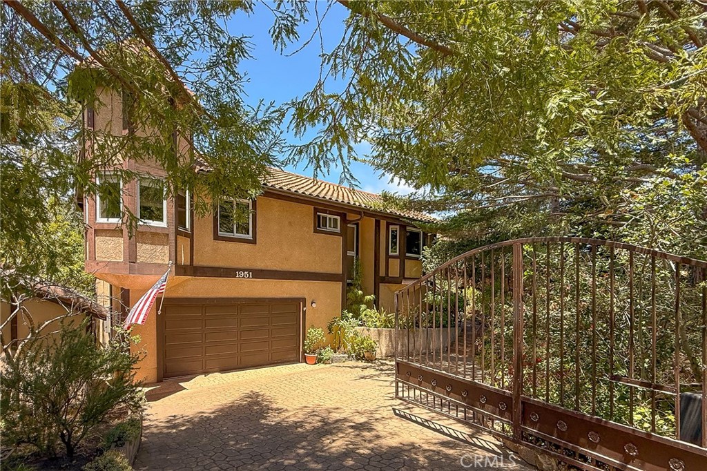 Two-story tan house with a tiled roof, two-car garage, and open metal driveway gate.