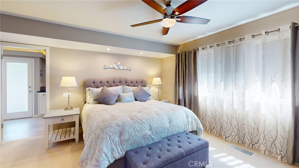 Bedroom with a tufted bed, cushioned bench, ceiling fan, and large curtained windows.