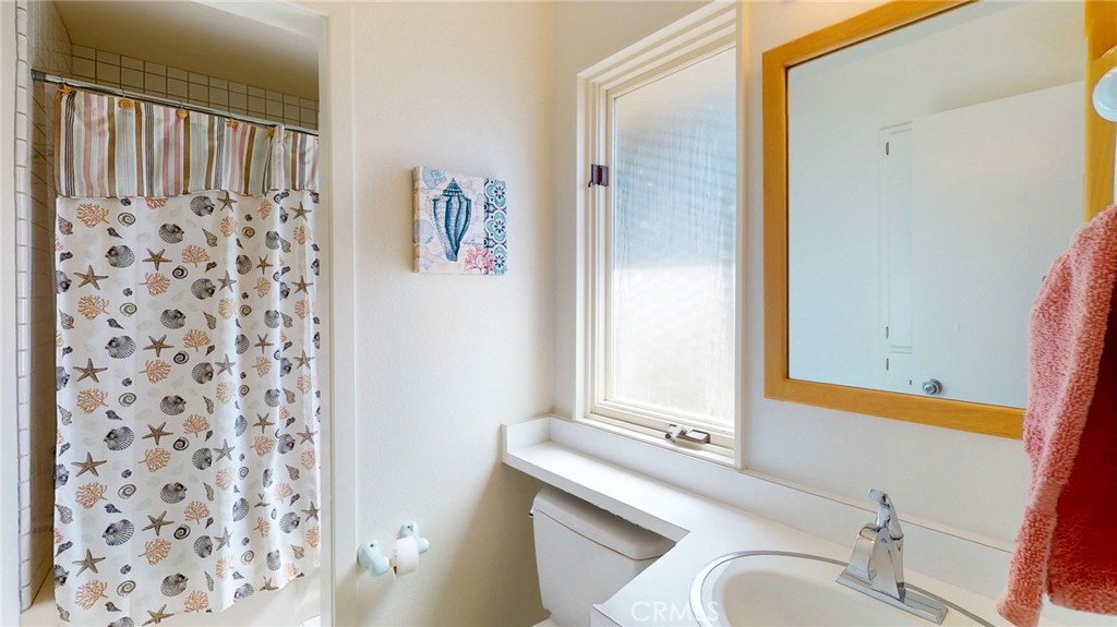 Bathroom with a white vanity, wood-framed mirror, and seashell-patterned shower curtain.