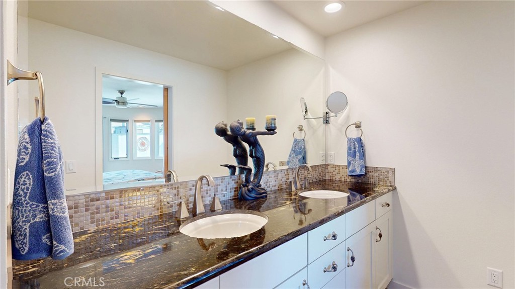 Bathroom vanity with two vessel sinks, dark stone countertop, mosaic tile backsplash, and blue towels.