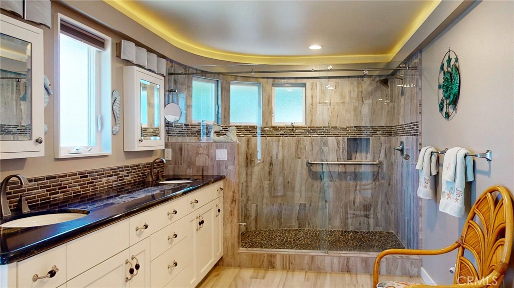Bathroom with a long double-sink vanity and a spacious stone-tiled walk-in shower.
