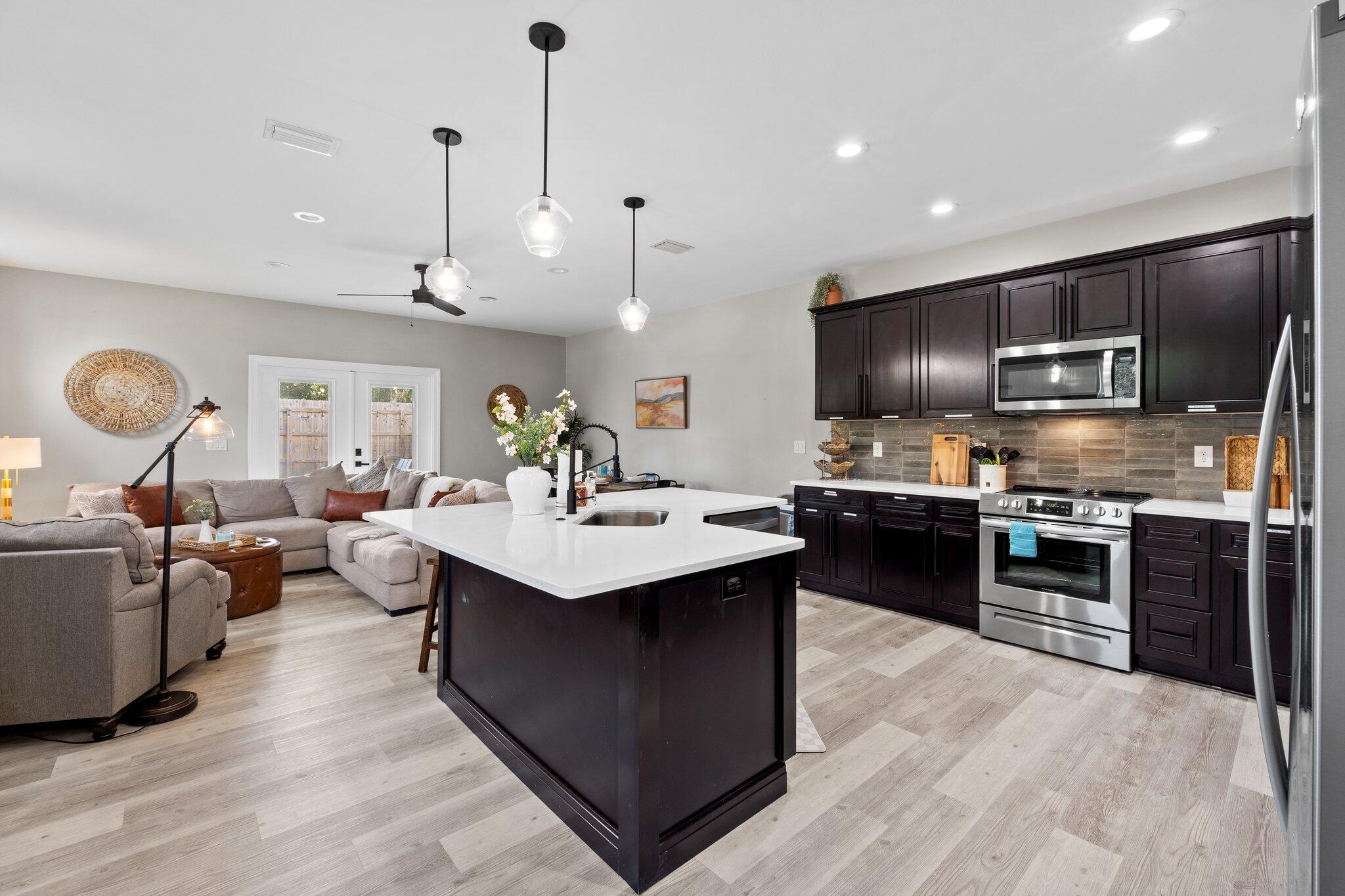 Open-plan kitchen with a large white island, dark cabinets, stainless steel appliances, and a gray sectional.