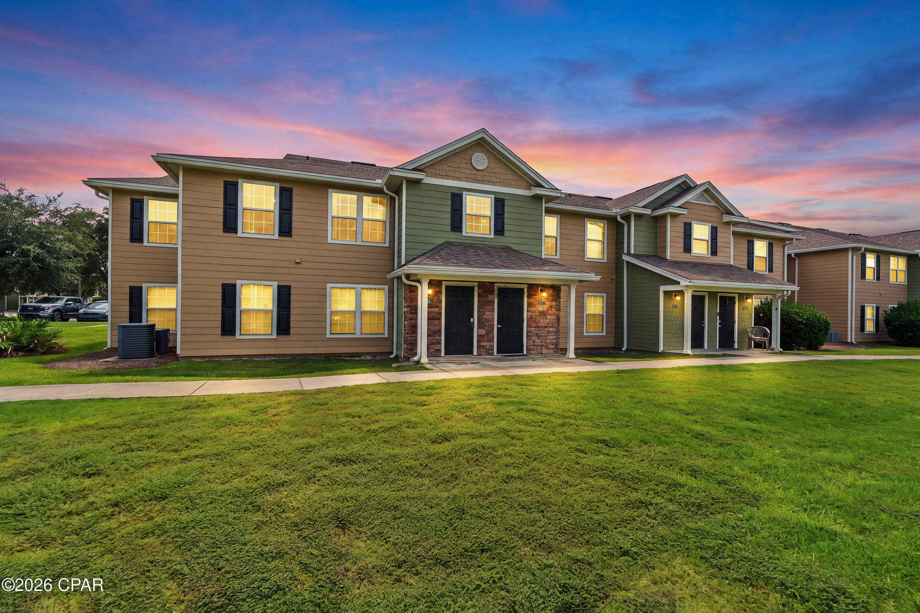 Attached two-story townhomes with brick entries and glowing windows at dusk.