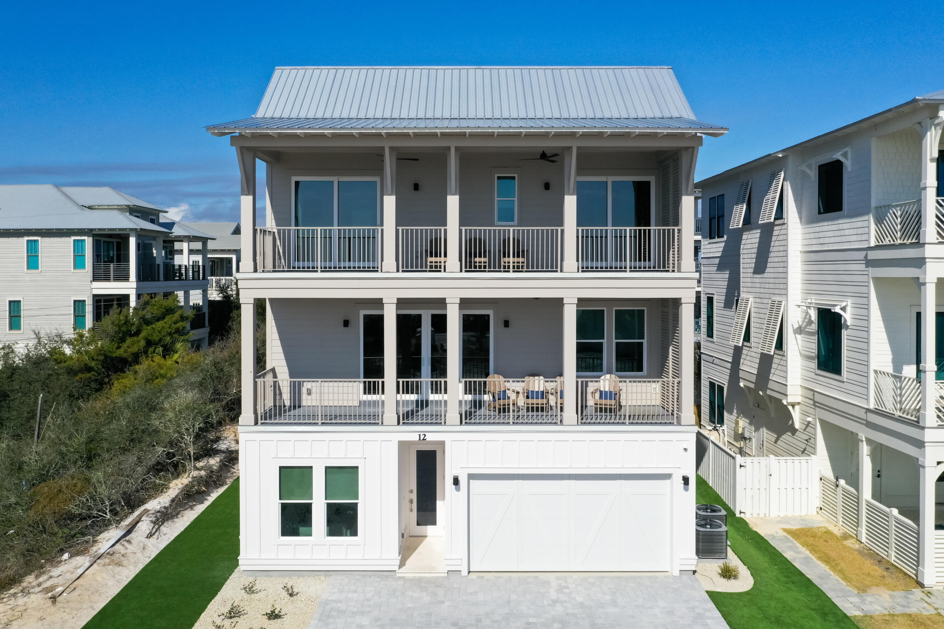 White three-story coastal home with two covered balconies, outdoor seating, and a garage.
