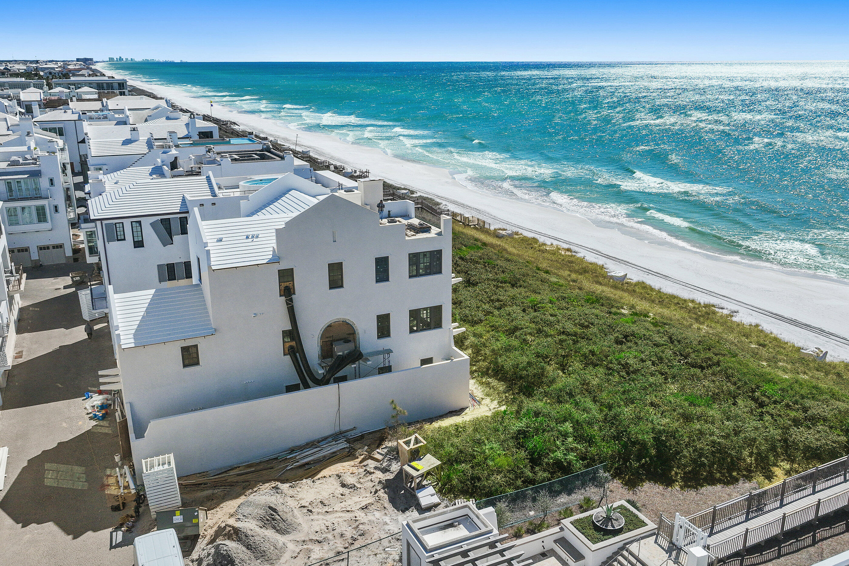 Aerial view of a beachfront home under construction beside white sand and turquoise water.