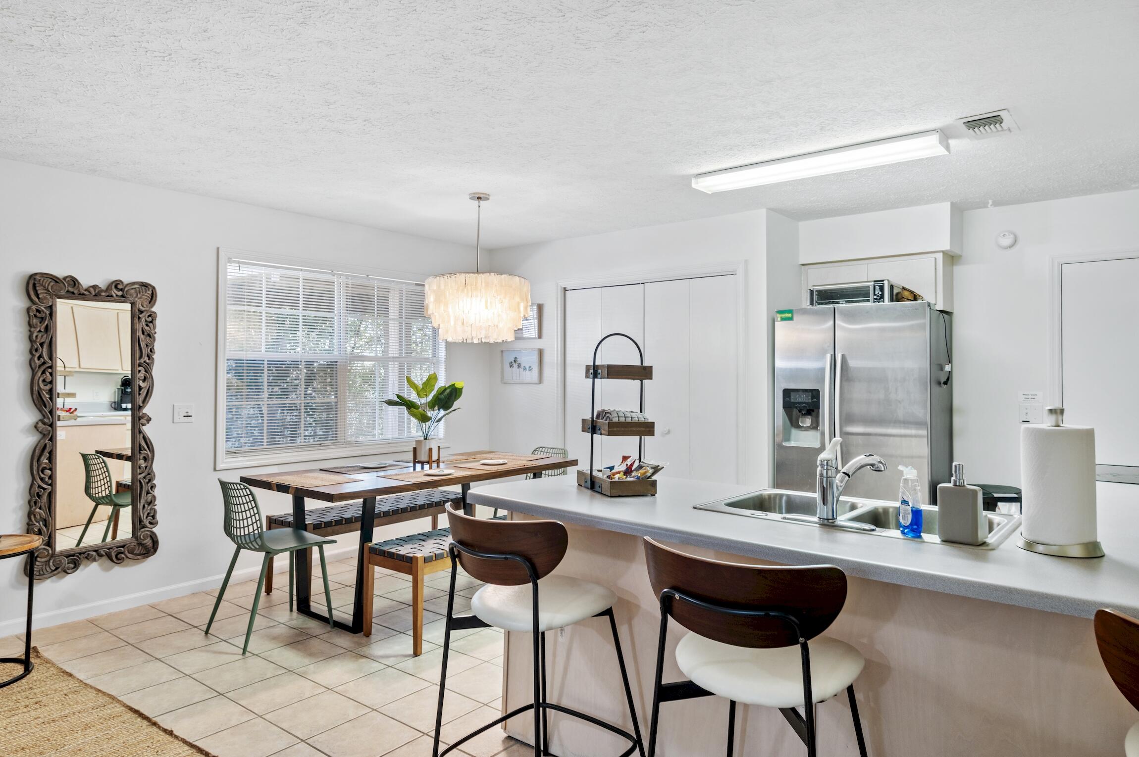 Kitchen and dining area with a white island, stainless steel refrigerator, and wooden dining table.