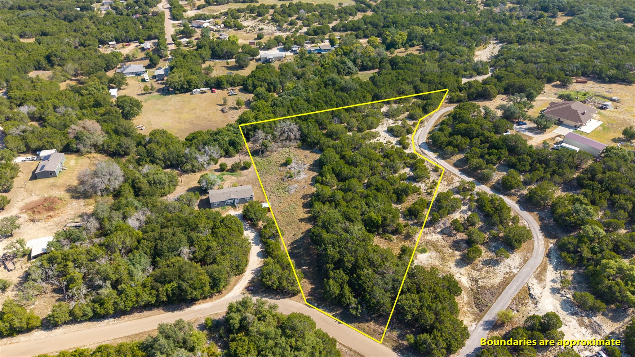 Wooded vacant lot outlined in yellow beside a curving road.