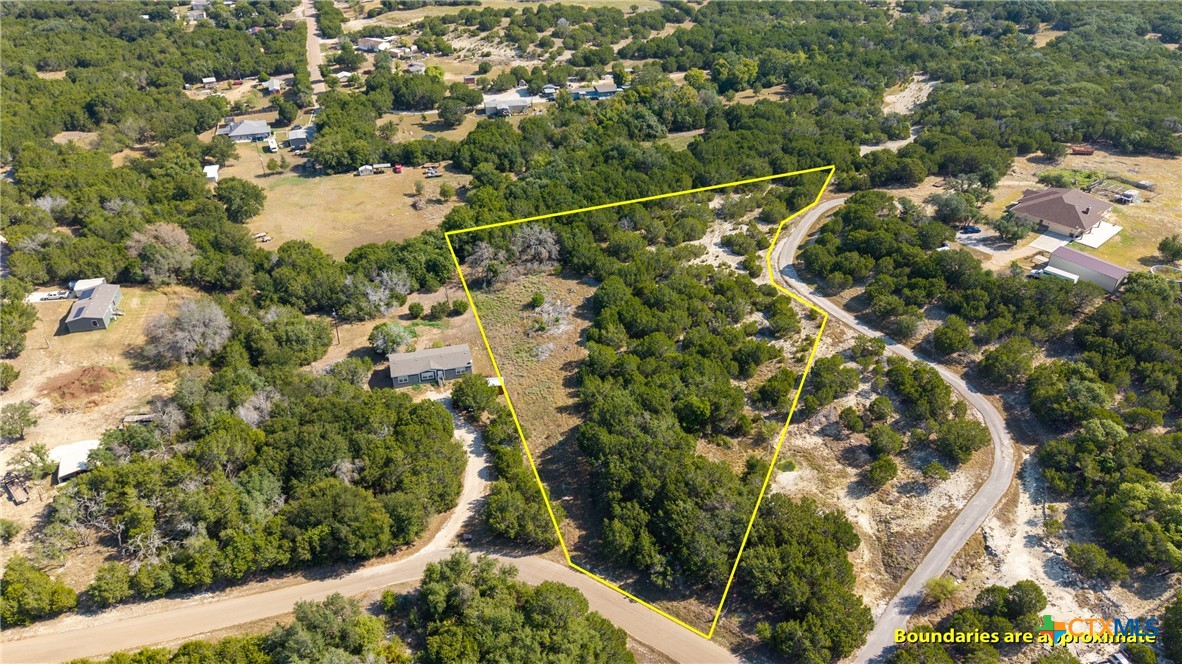 Aerial view of a wooded property outlined in yellow beside a curving road.