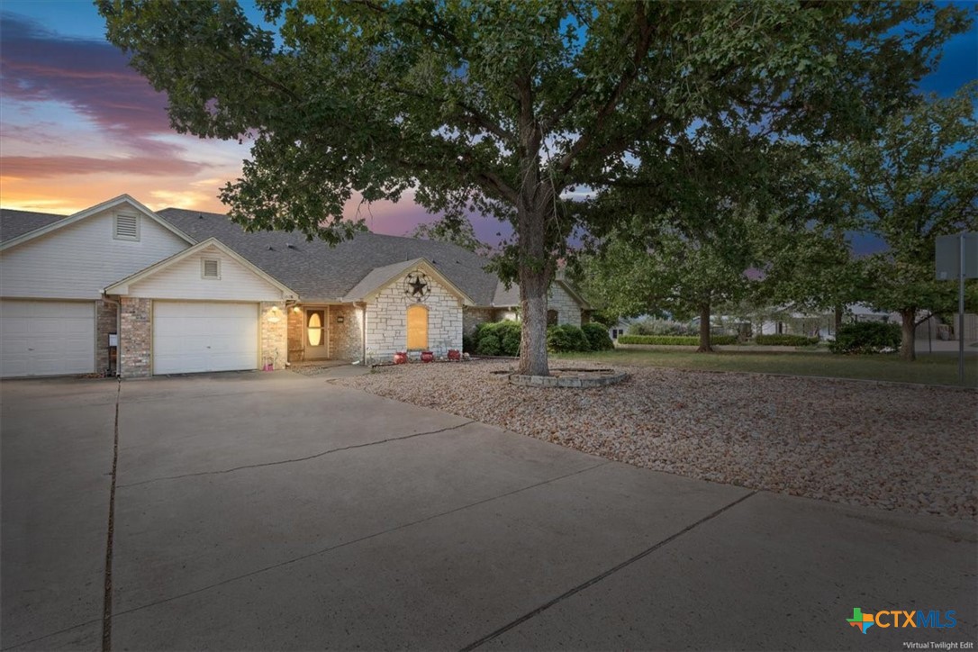 Single-story stone-and-siding home with two garage doors and a large tree at dusk.