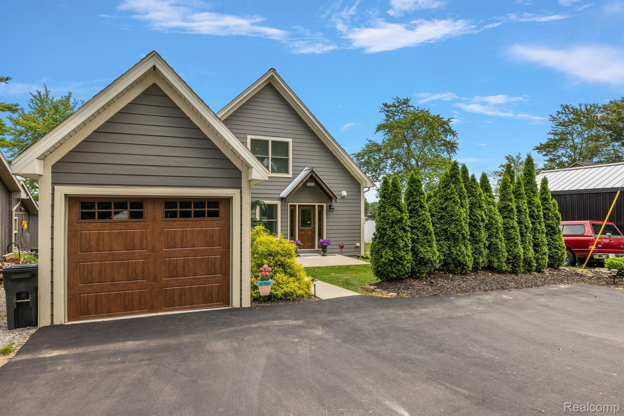 Gray two-story home with steep gables, a brown double garage door, and evergreen trees beside the driveway.