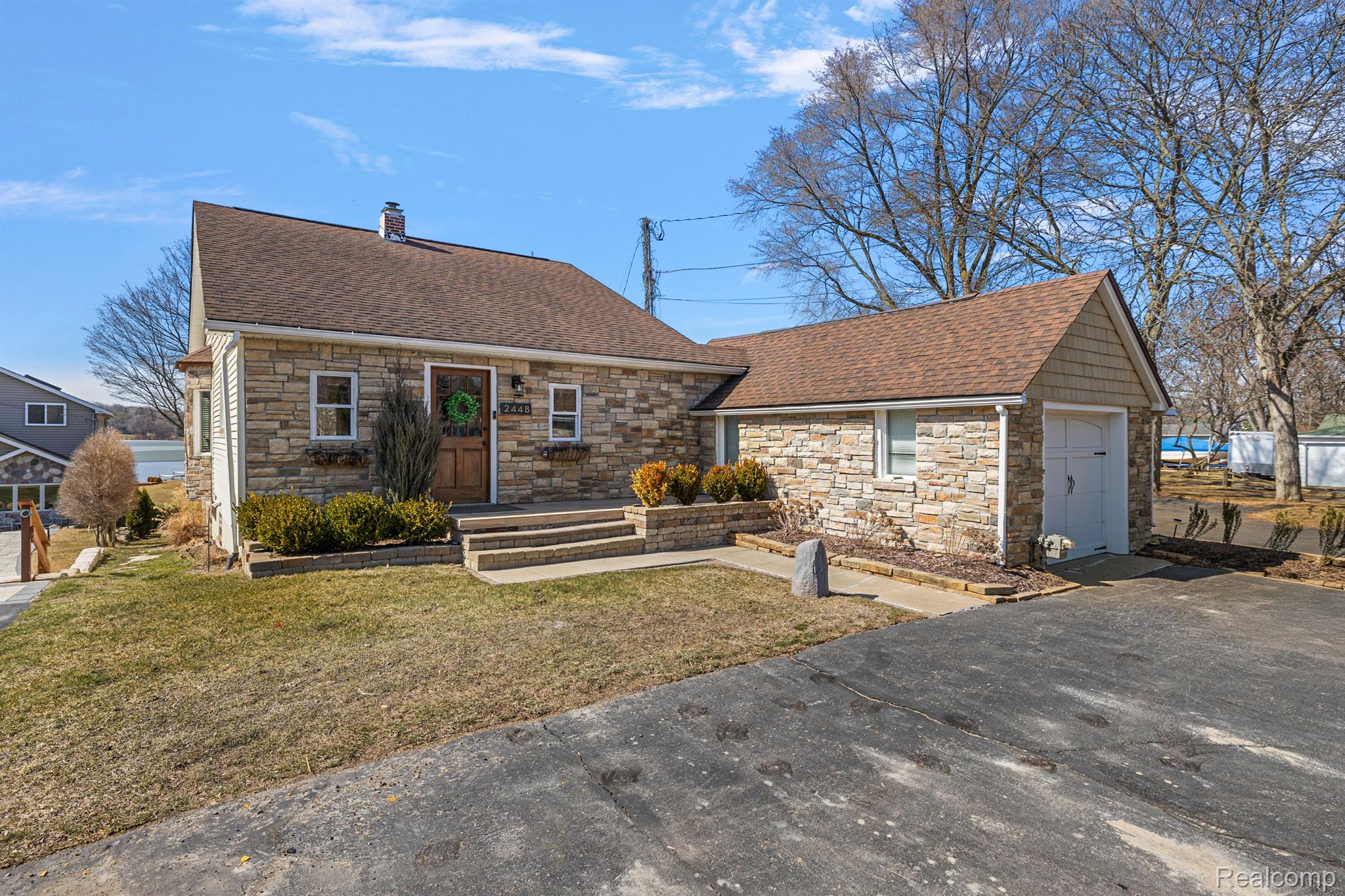 Stone-faced home with attached garage, front steps, and a glimpse of water nearby.