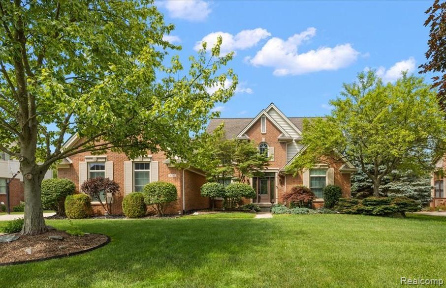 Two-story brick house with prominent gables, landscaped shrubs, and a broad lawn shaded by mature trees.