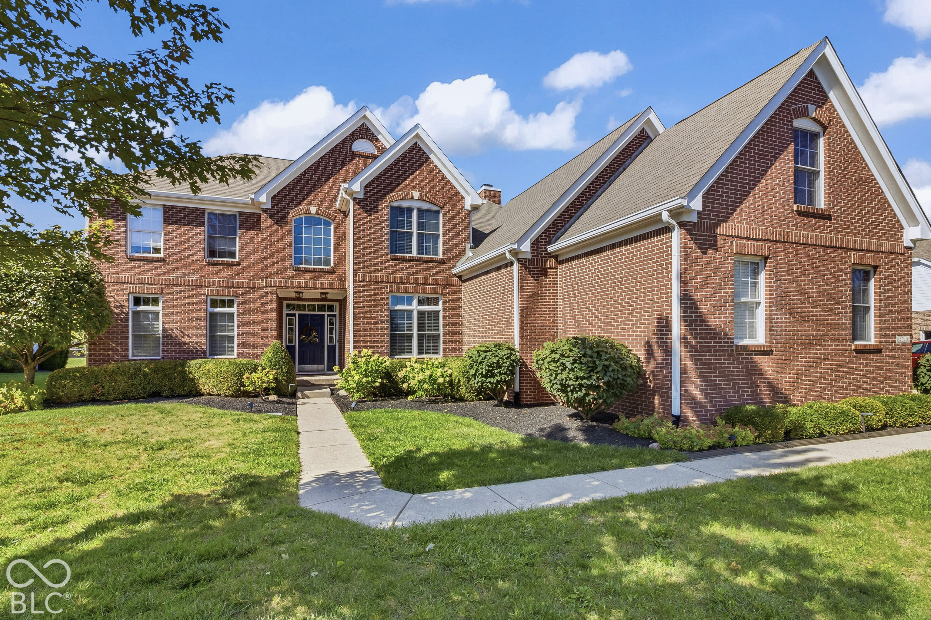 Two-story red brick home with multiple gables, landscaped lawn, and a central front walkway.