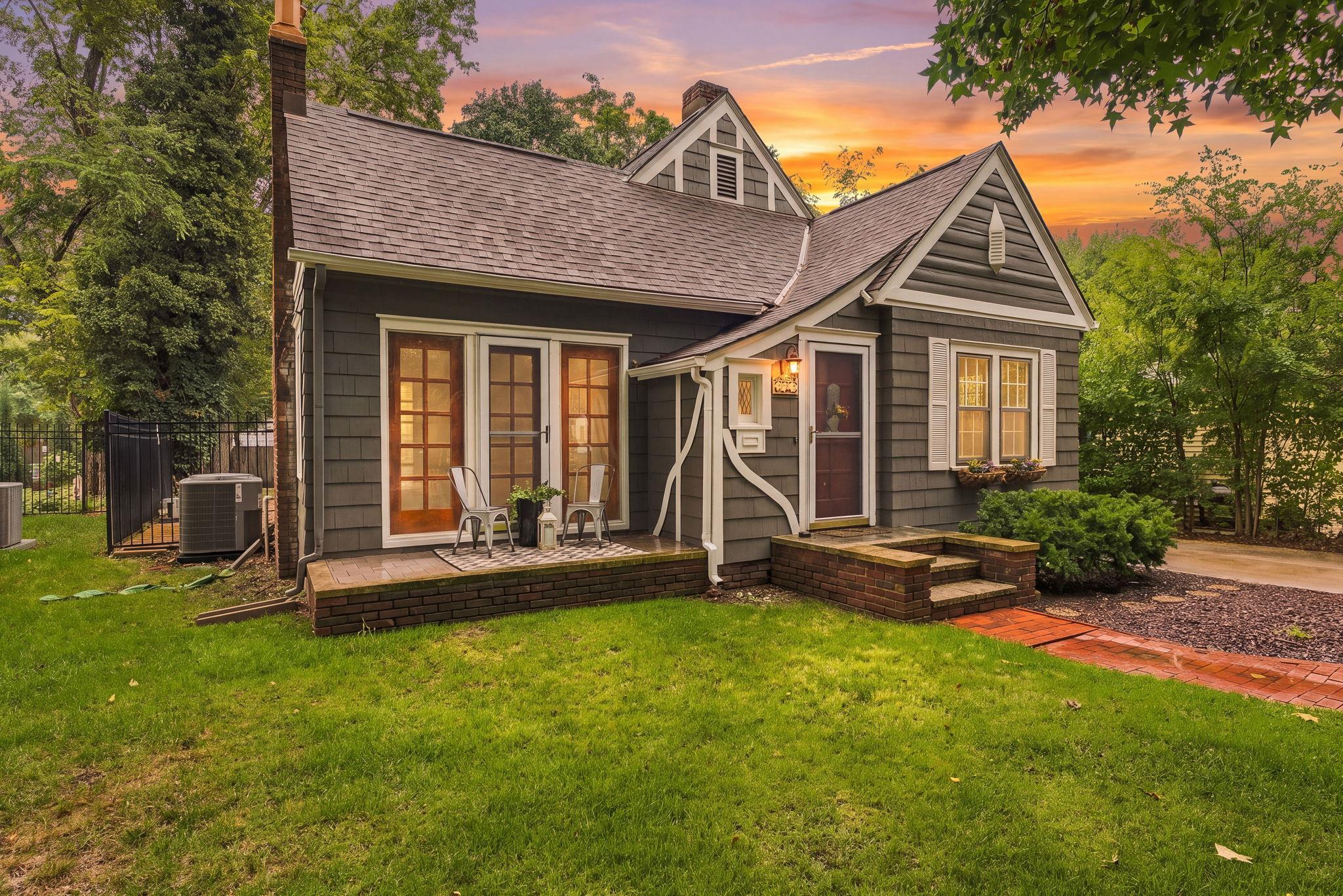 Gray gabled house with a raised brick porch and steps at sunset.