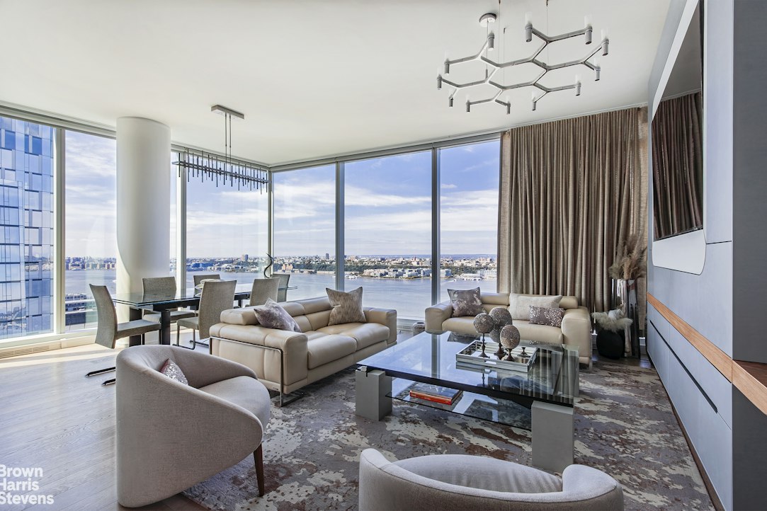 Furnished living room with floor-to-ceiling windows overlooking the river and city.
