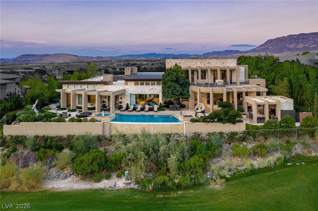 Modern luxury home with a pool and landscaped grounds, backed by distant mountains at dusk.
