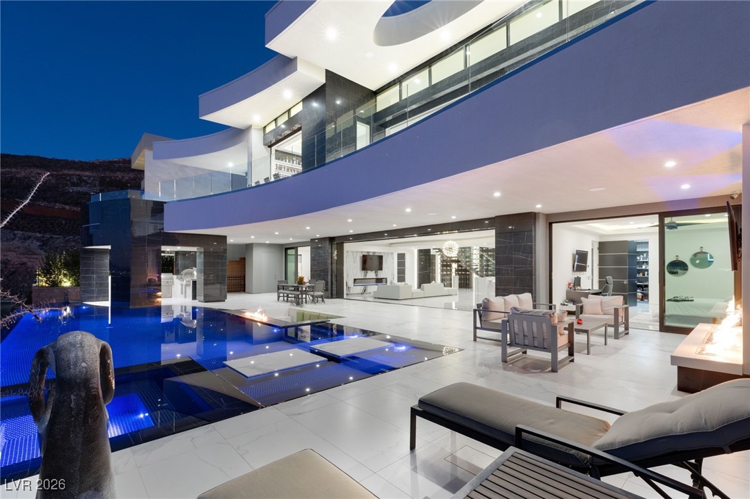 Modern home at night with a covered patio, outdoor seating, and blue-lit swimming pool.