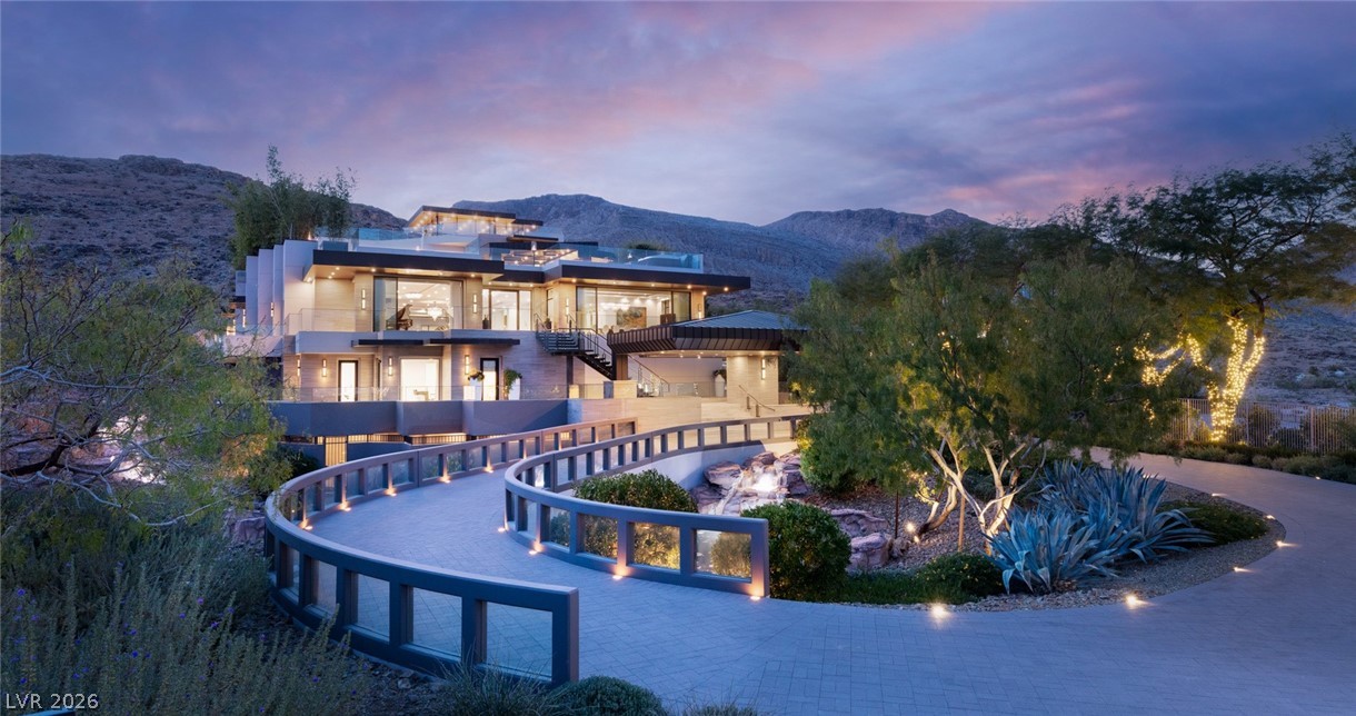 Modern multi-level home with a curved walkway and desert landscaping at dusk.