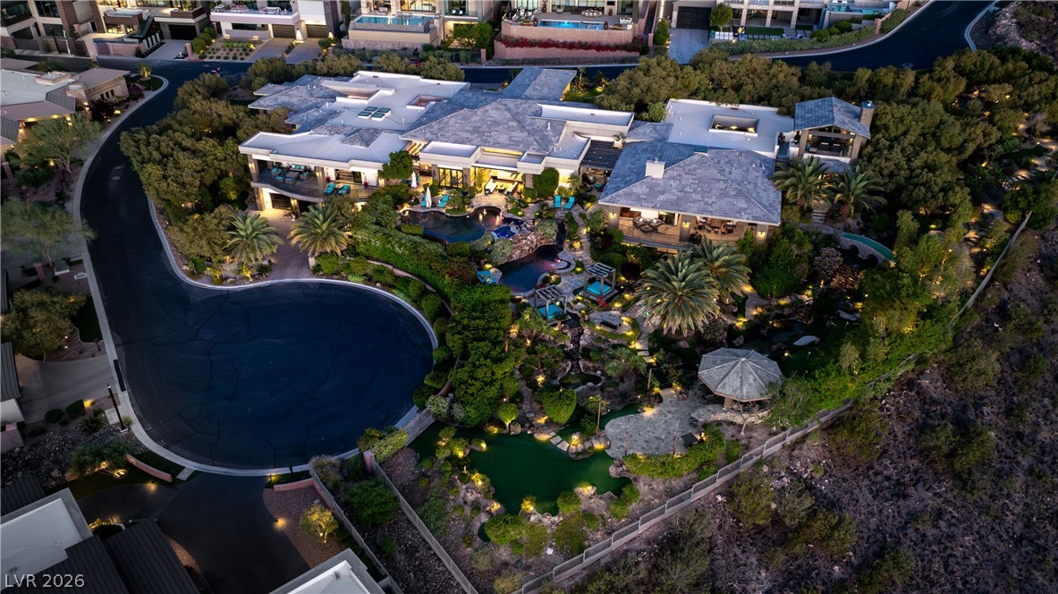 Luxury home with multiple pools, landscaped grounds, and a gazebo, seen from above at dusk.