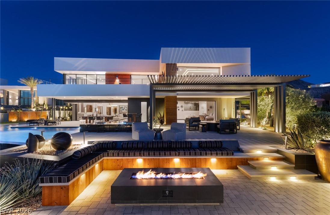 Modern two-story home at dusk with a pool, fire pit, and illuminated patio.