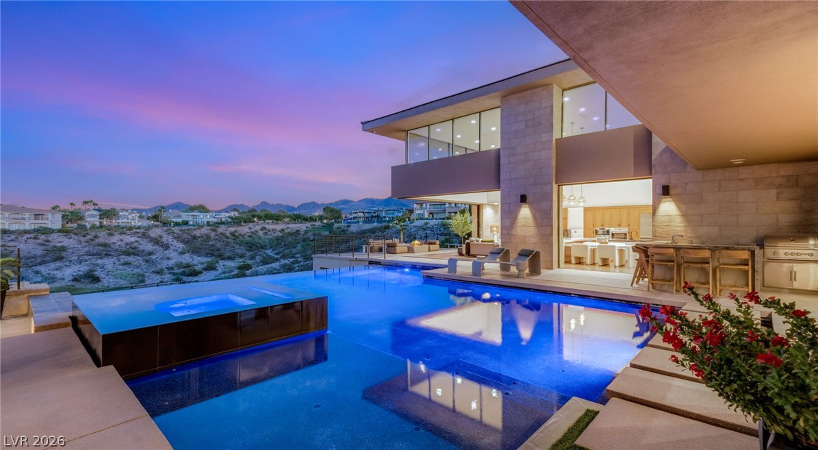 Modern Las Vegas home with an illuminated pool and raised spa at dusk.