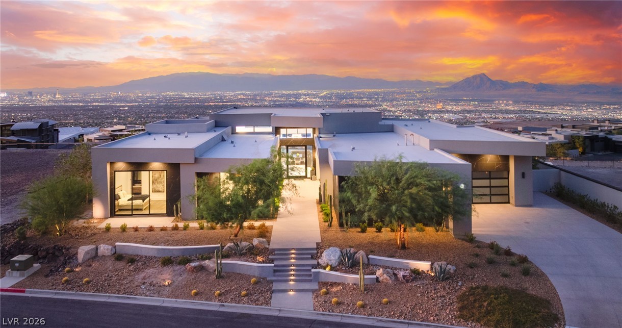 Modern flat-roofed home with desert landscaping, Las Vegas lights and mountains at dusk.