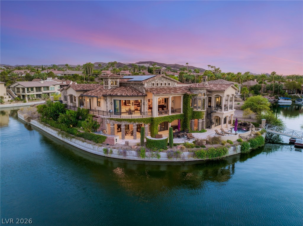 Waterfront home on a canal, with tile roofs and landscaped grounds at dusk.