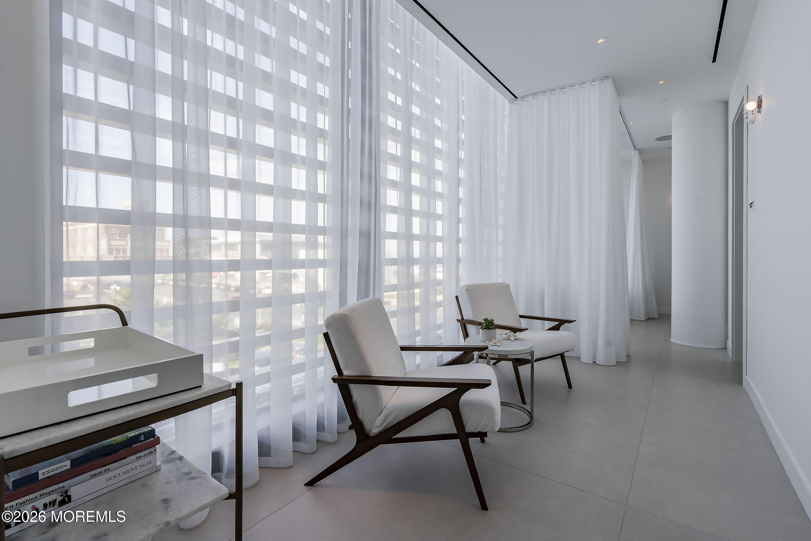 Modern sitting area with white lounge chairs, sheer curtains, and floor-to-ceiling windows.