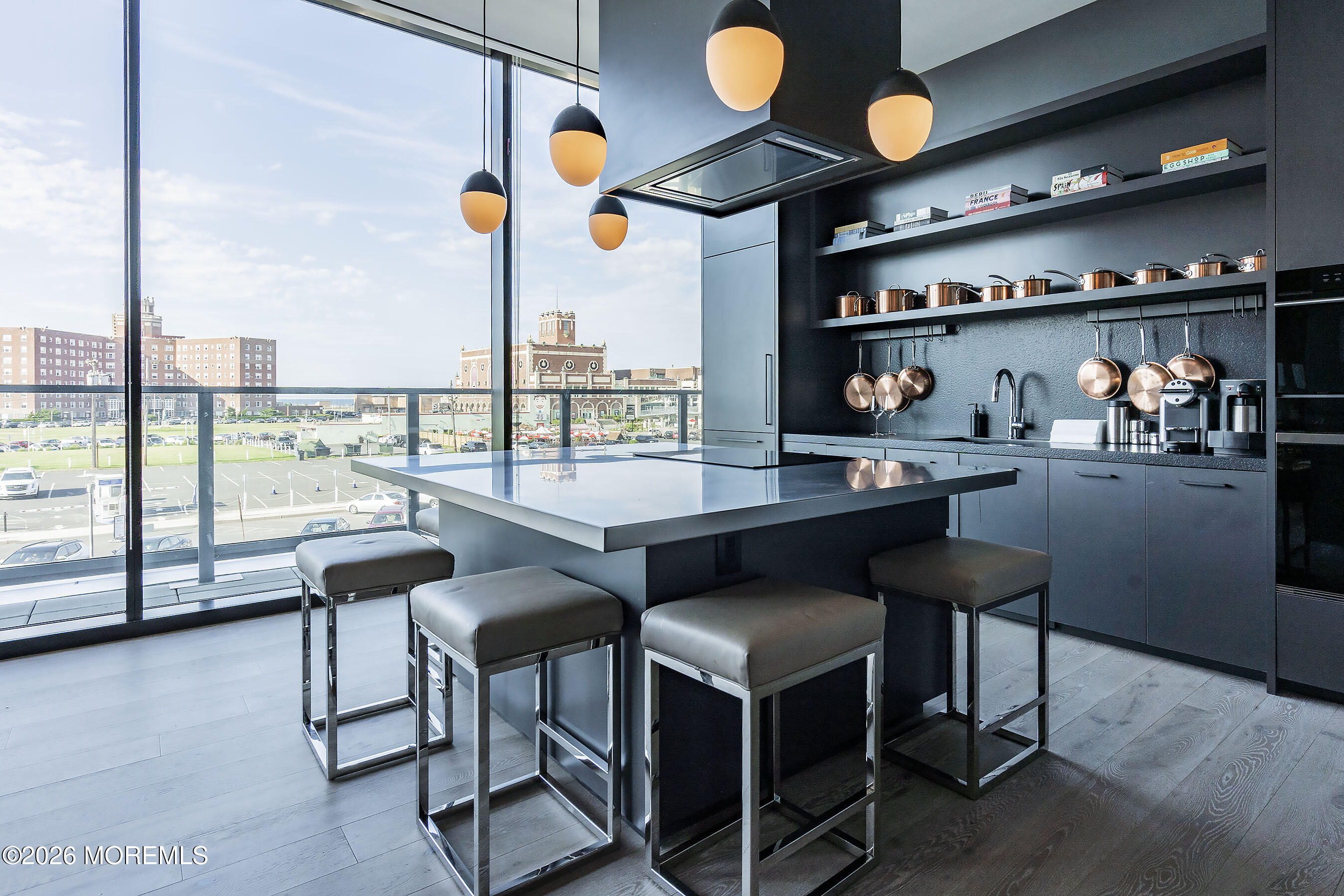 Modern kitchen with dark cabinetry, an island and stools beside floor-to-ceiling windows overlooking the city.