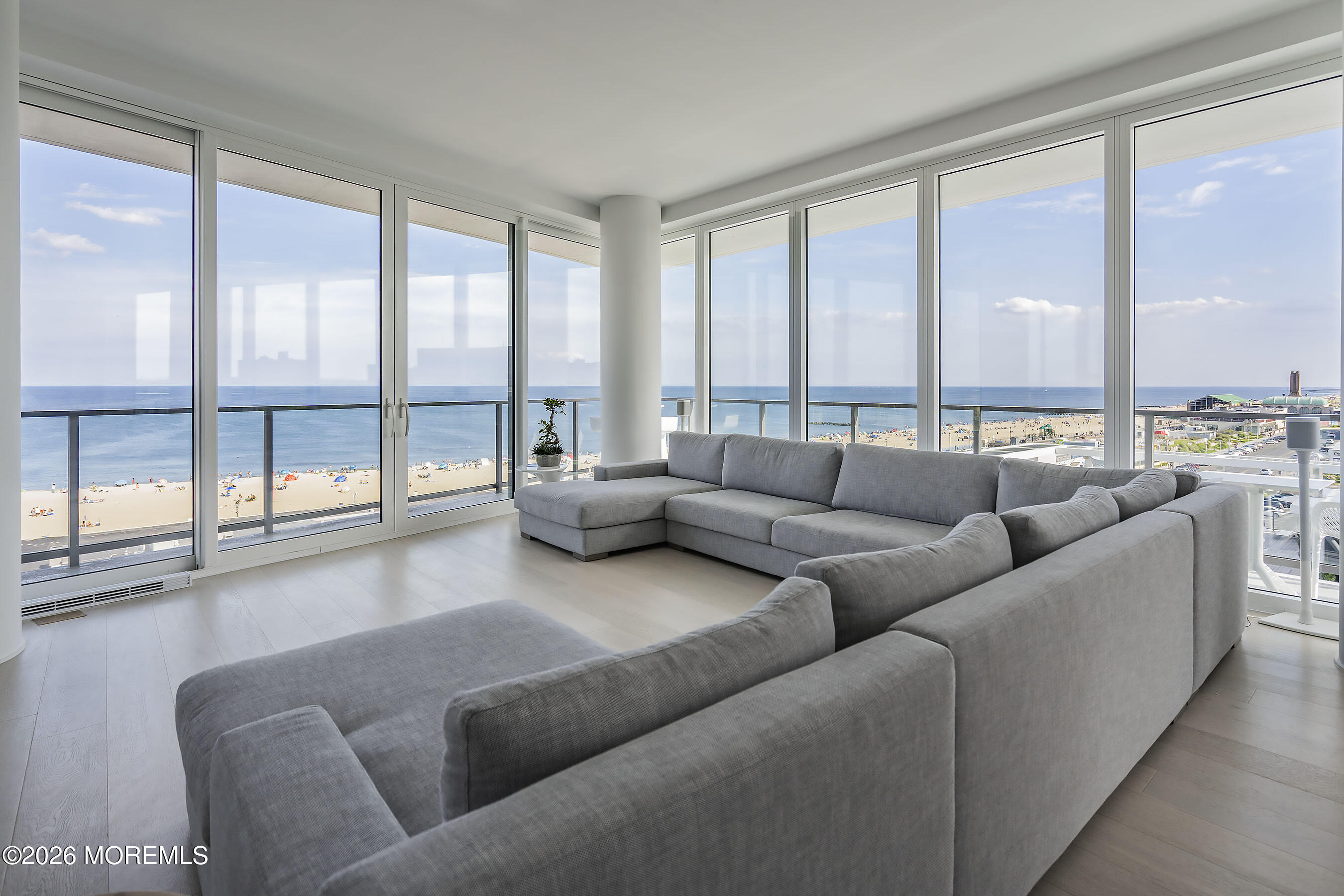 Living room with a large gray sectional and floor-to-ceiling windows overlooking the ocean and beach.