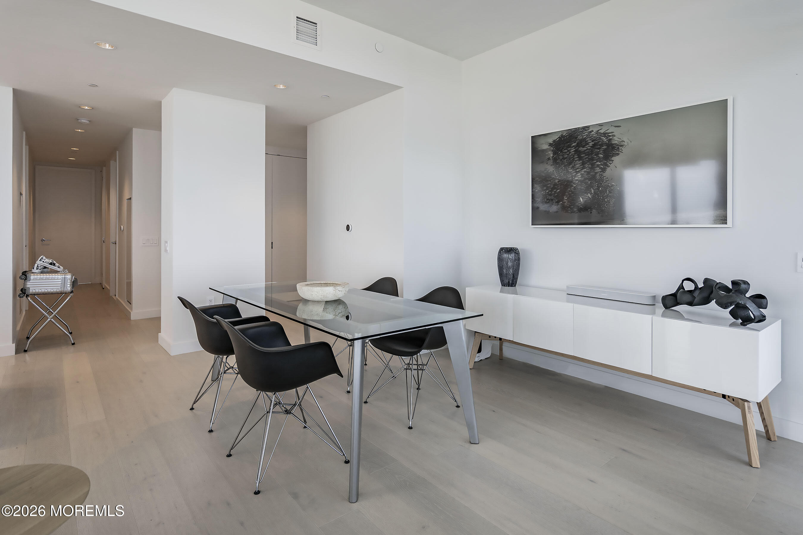 Modern dining area with a glass table, black chairs, and a white sideboard.