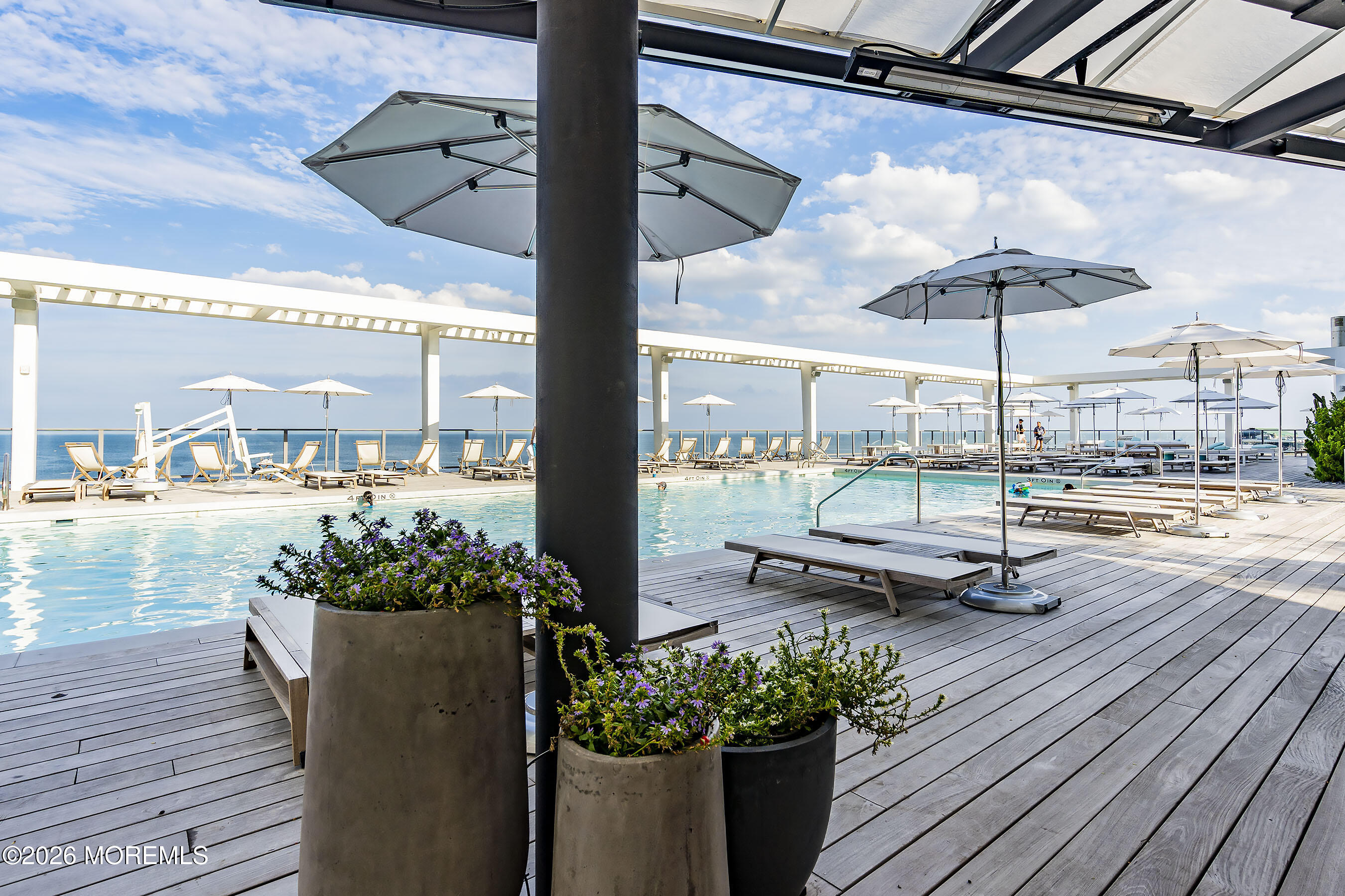 Oceanfront pool deck with lounge chairs, umbrellas, and large planters.