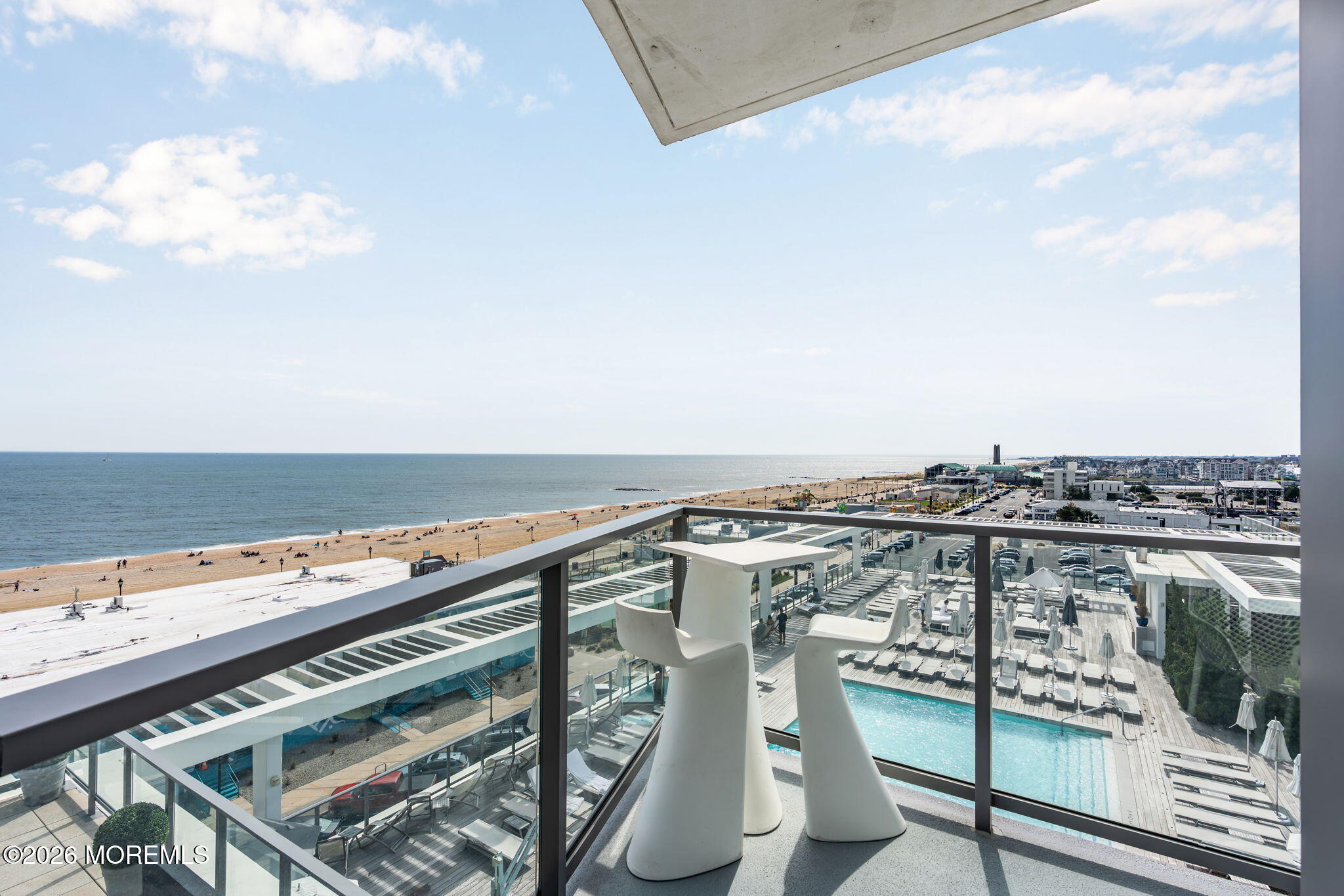 Balcony overlooking the ocean, beach, and swimming pool, with sculptural white chairs in the foreground.