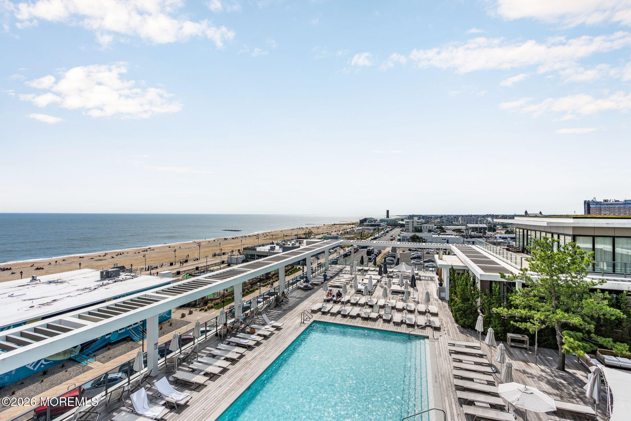Rooftop pool deck overlooking the beach and ocean, with lounge chairs and white pergolas.