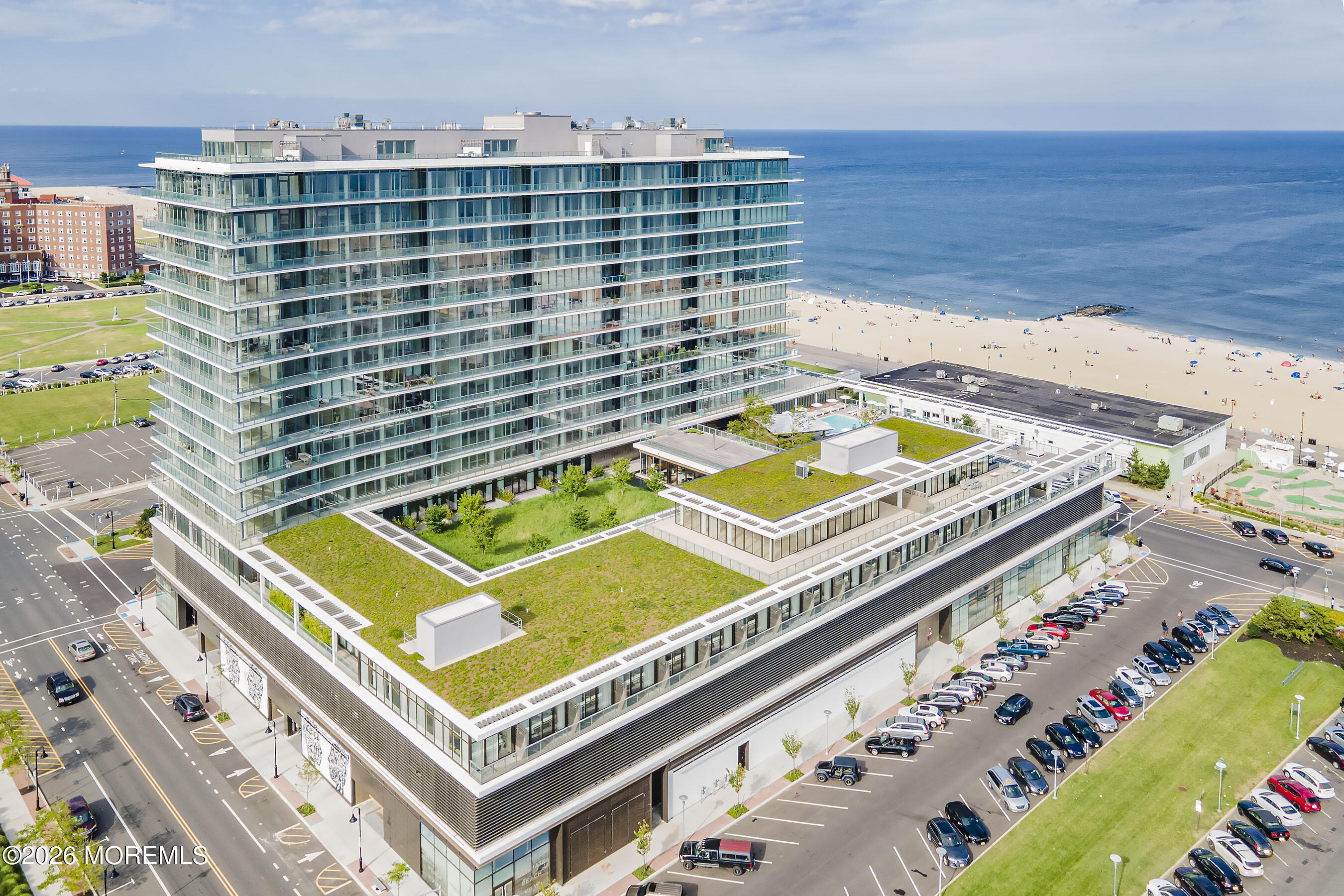 Modern beachfront condominium with green rooftops beside a sandy beach and ocean.