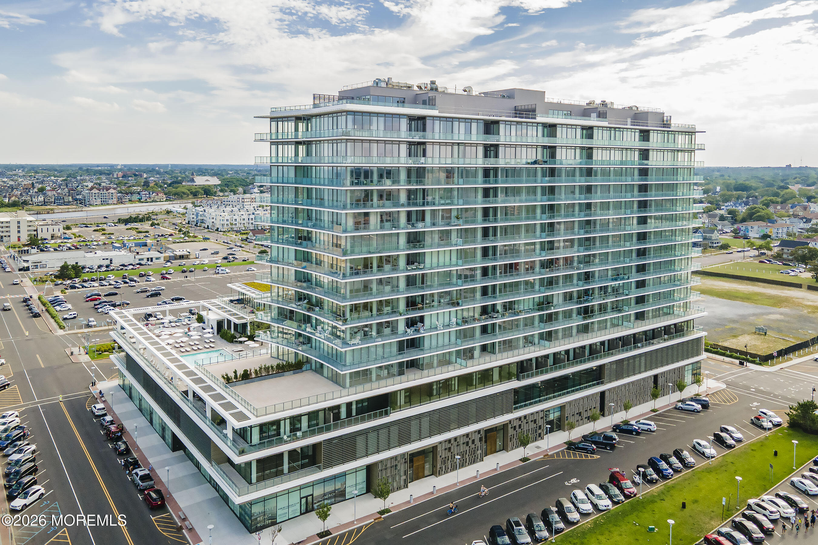 Modern glass condominium tower with wraparound balconies and a pool terrace, viewed from above.
