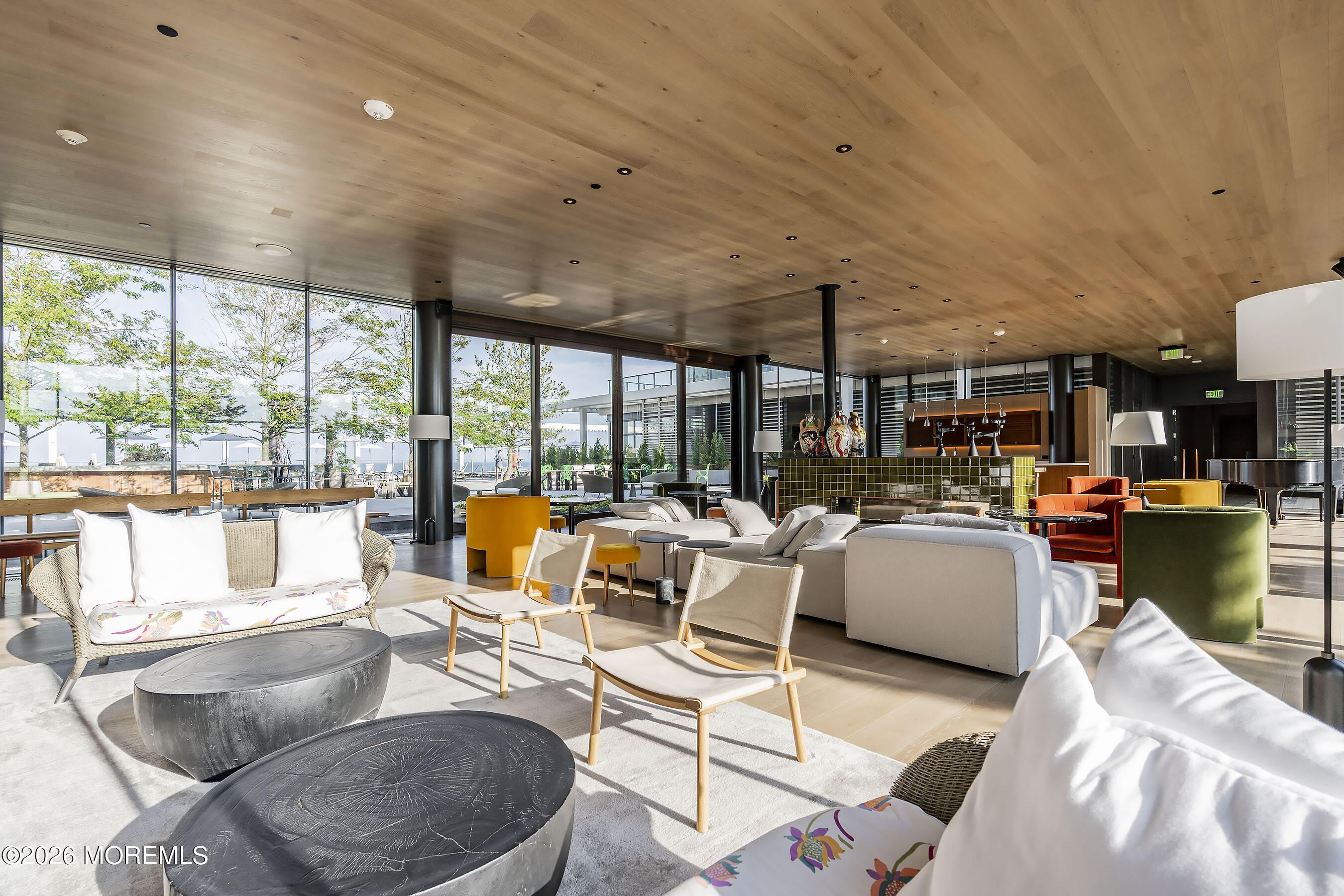 Furnished lounge with floor-to-ceiling windows, sculptural coffee tables, and colorful seating.