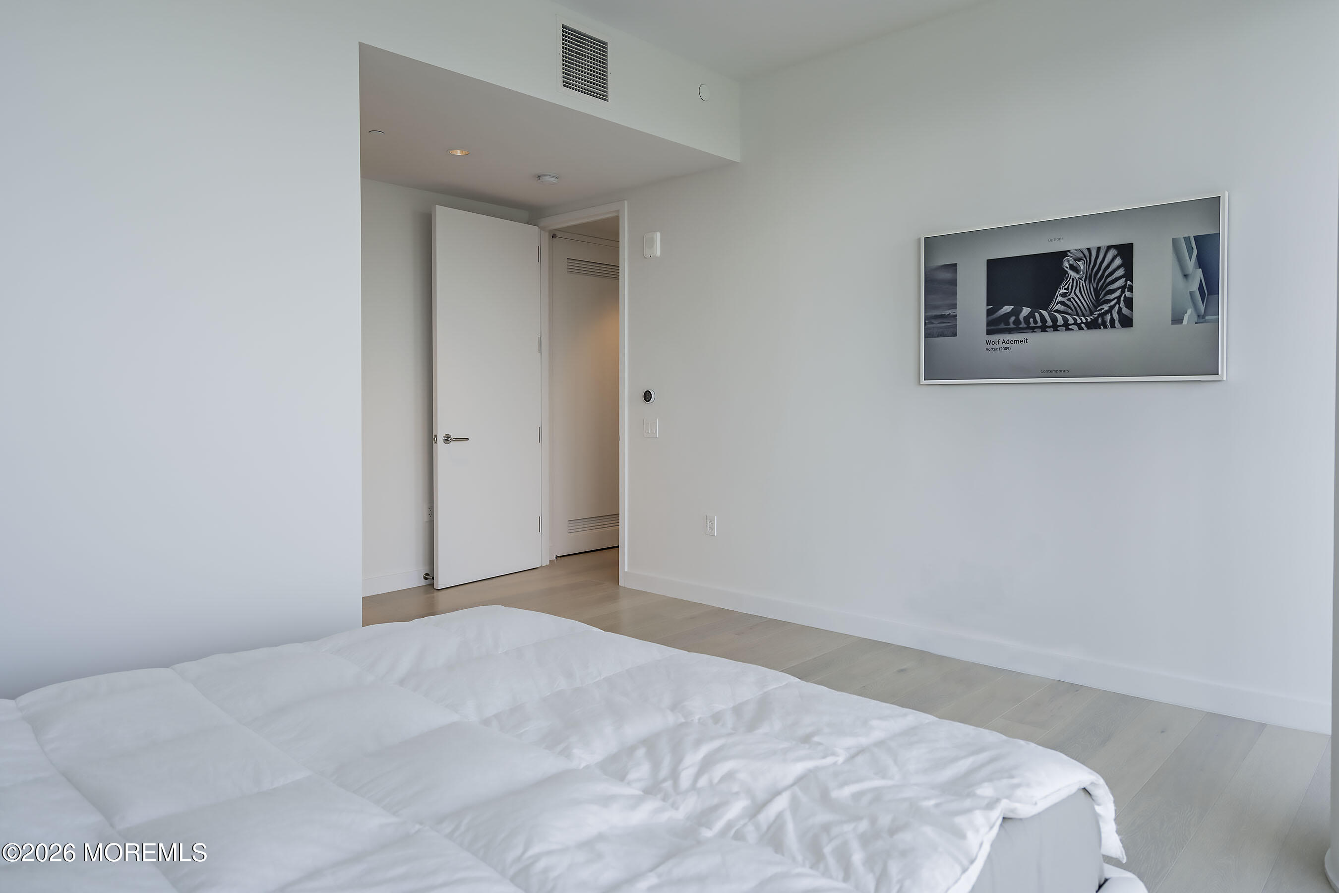 Modern bedroom with a white bed, pale wood floors, and framed zebra artwork.