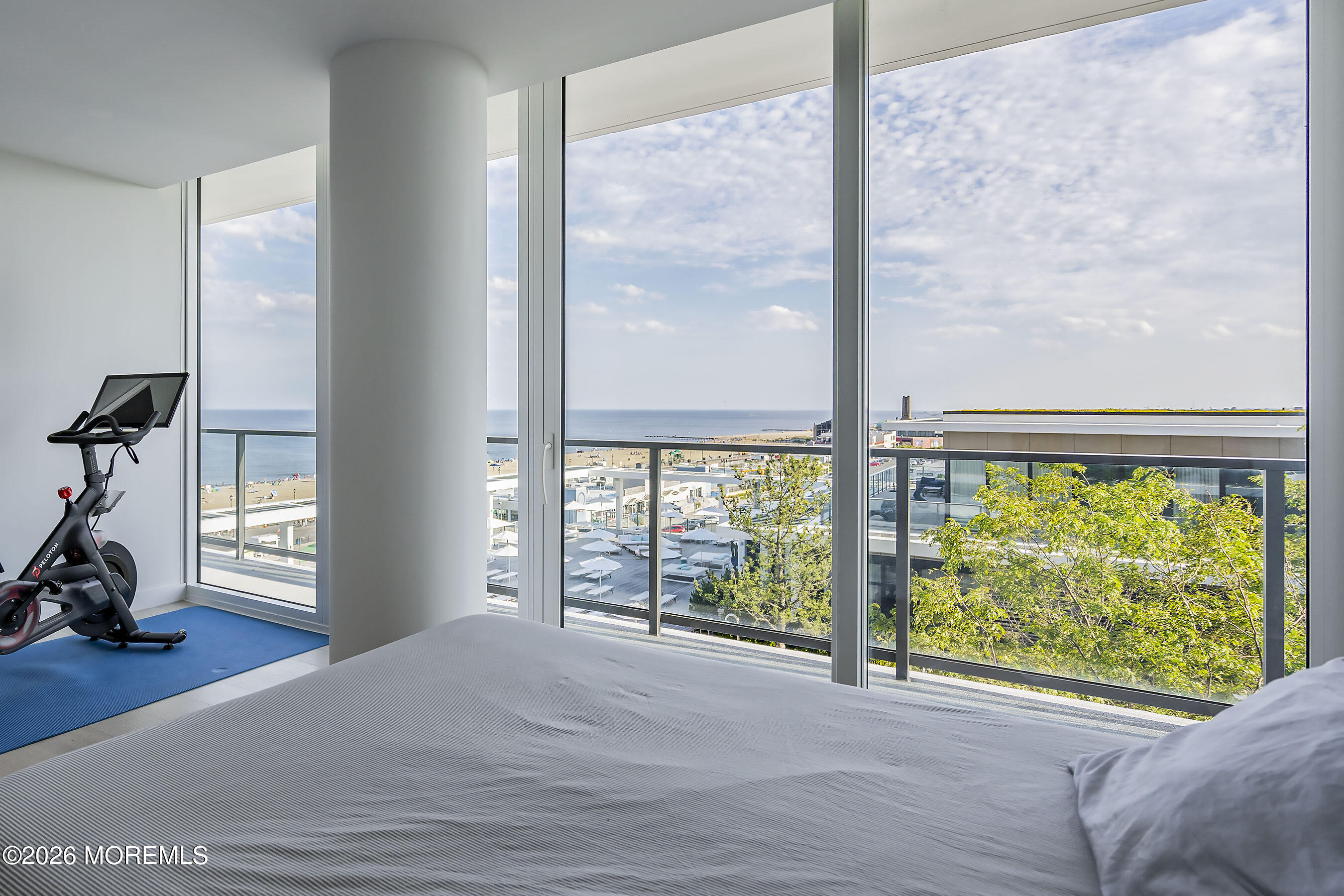 Bedroom with floor-to-ceiling ocean-view windows, a bed, and an exercise bike.