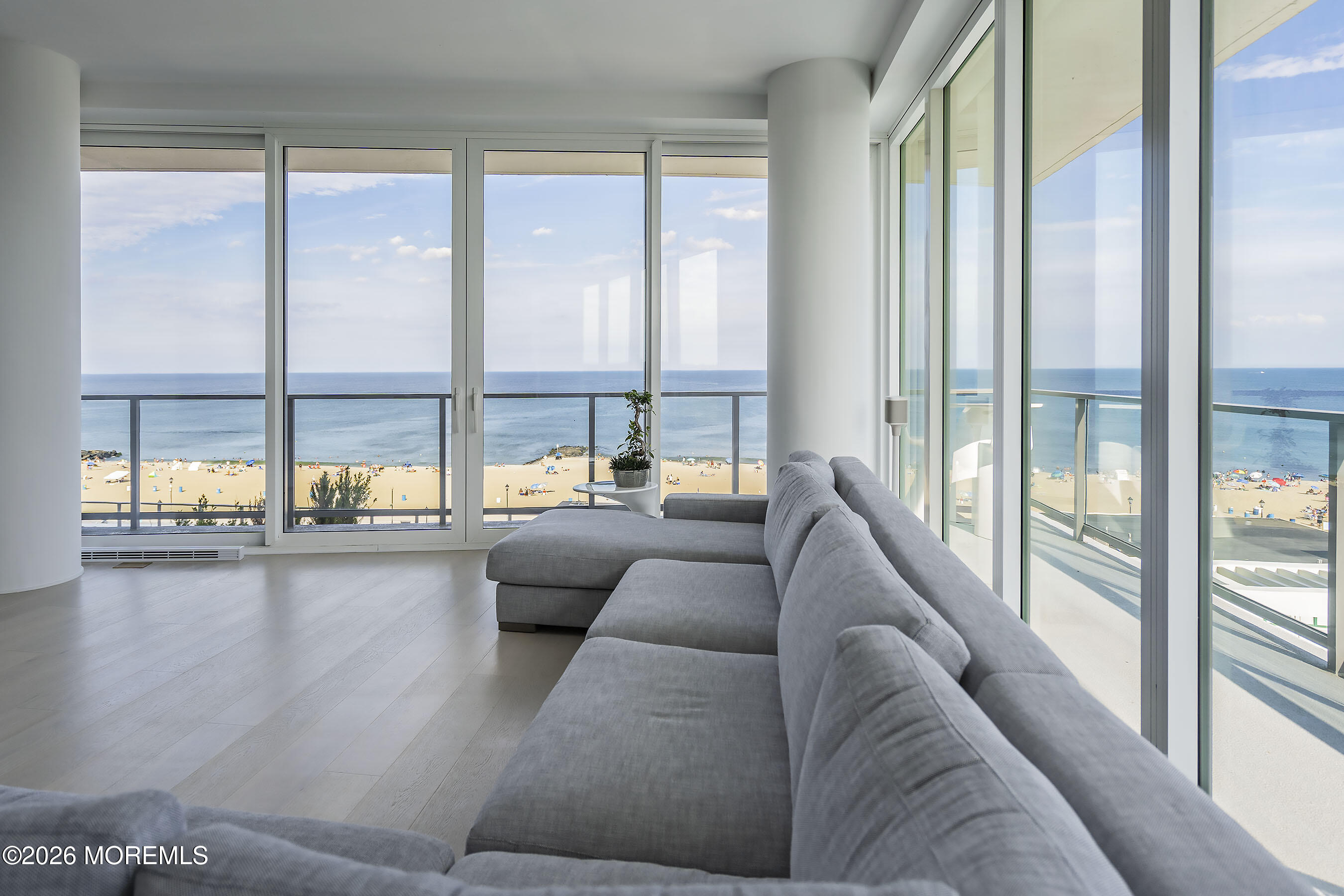 Living room with a gray sectional and panoramic windows overlooking the beach and ocean.