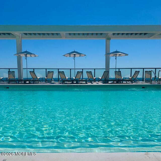 Outdoor pool with turquoise water, lounge chairs, umbrellas, and a pergola overlooking the water.