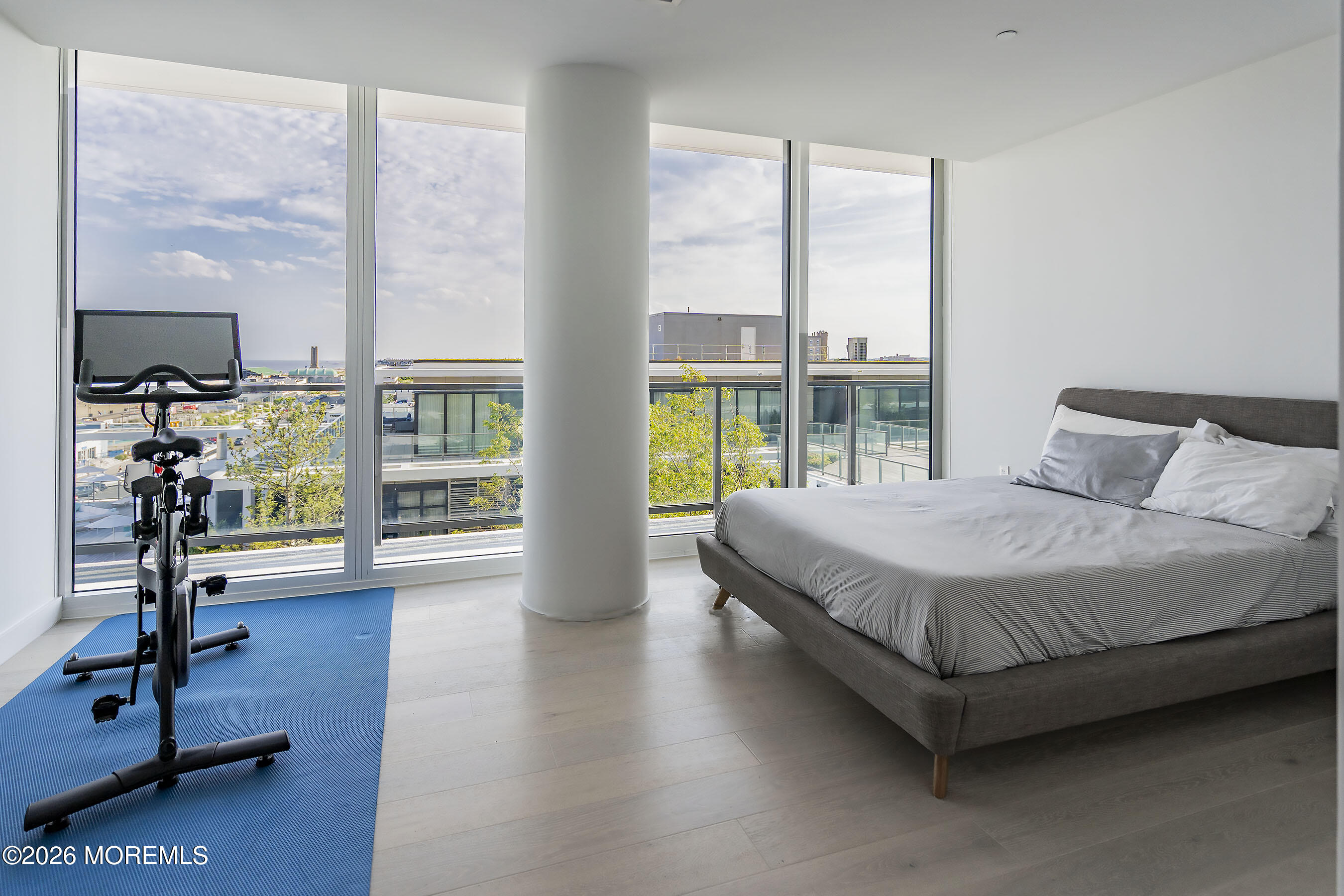 Bedroom with floor-to-ceiling windows, a gray bed, and an exercise bike on a blue mat.