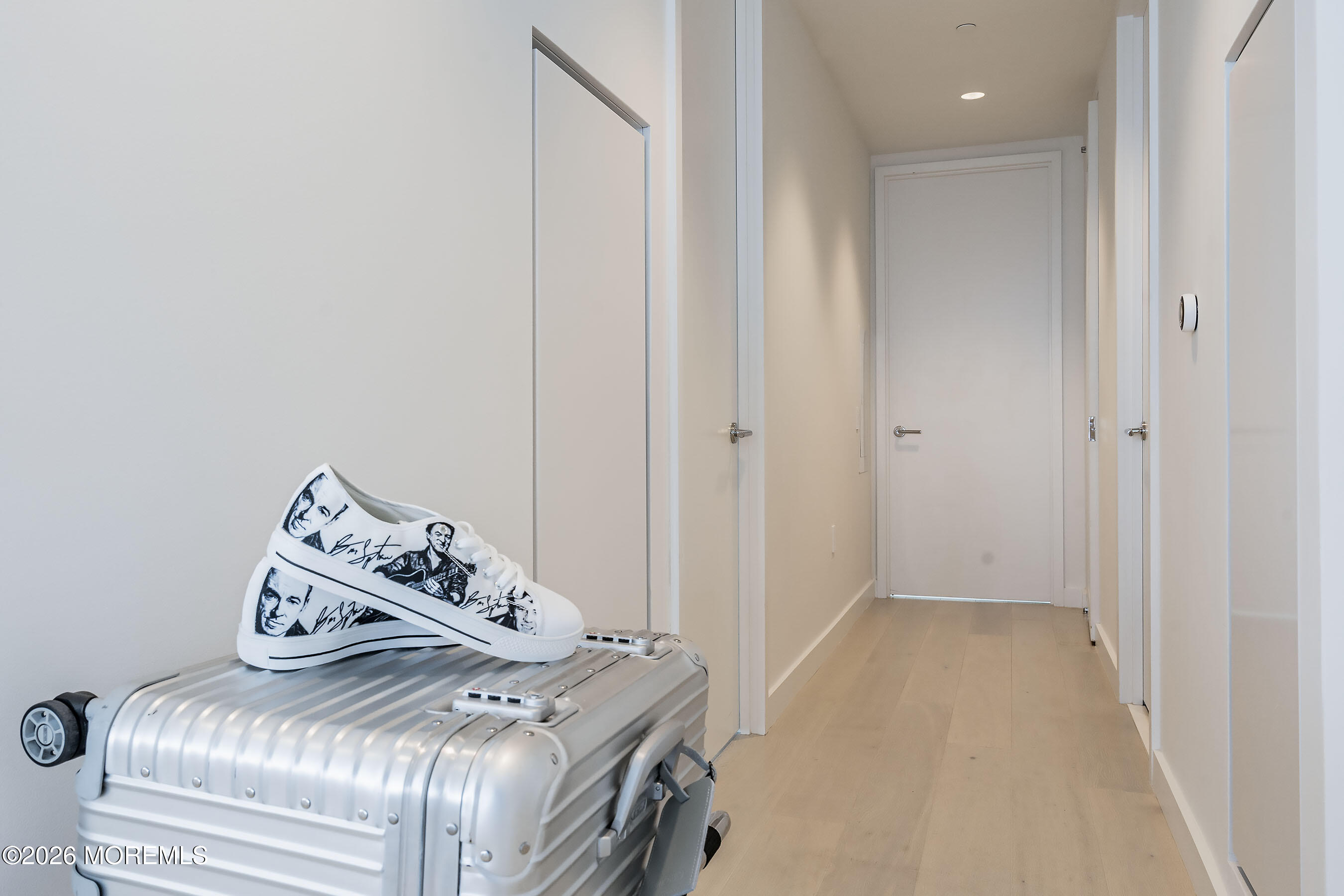 Apartment hallway with a silver suitcase and illustrated white sneakers in the foreground.