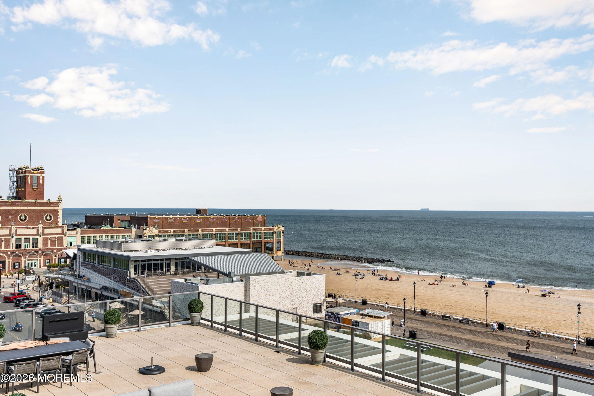Oceanfront terrace overlooking Asbury Park beach, boardwalk, and ocean, with glass railings and outdoor seating.