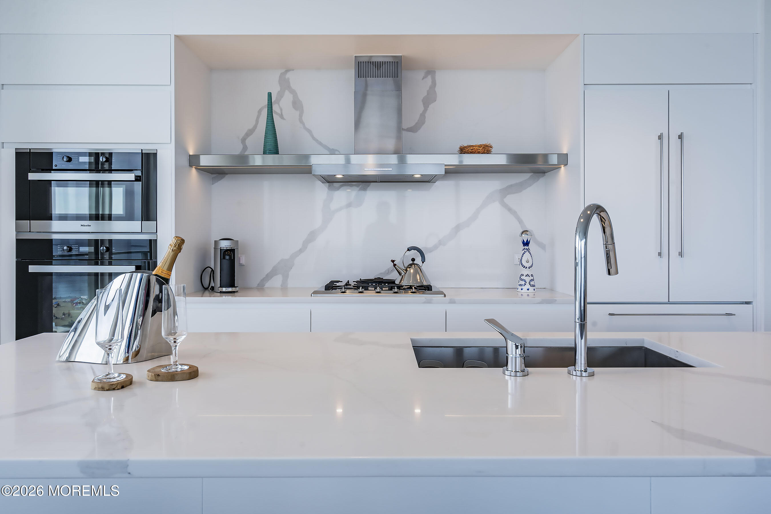 Modern white kitchen with a quartz island, stainless-steel appliances, and champagne glasses.