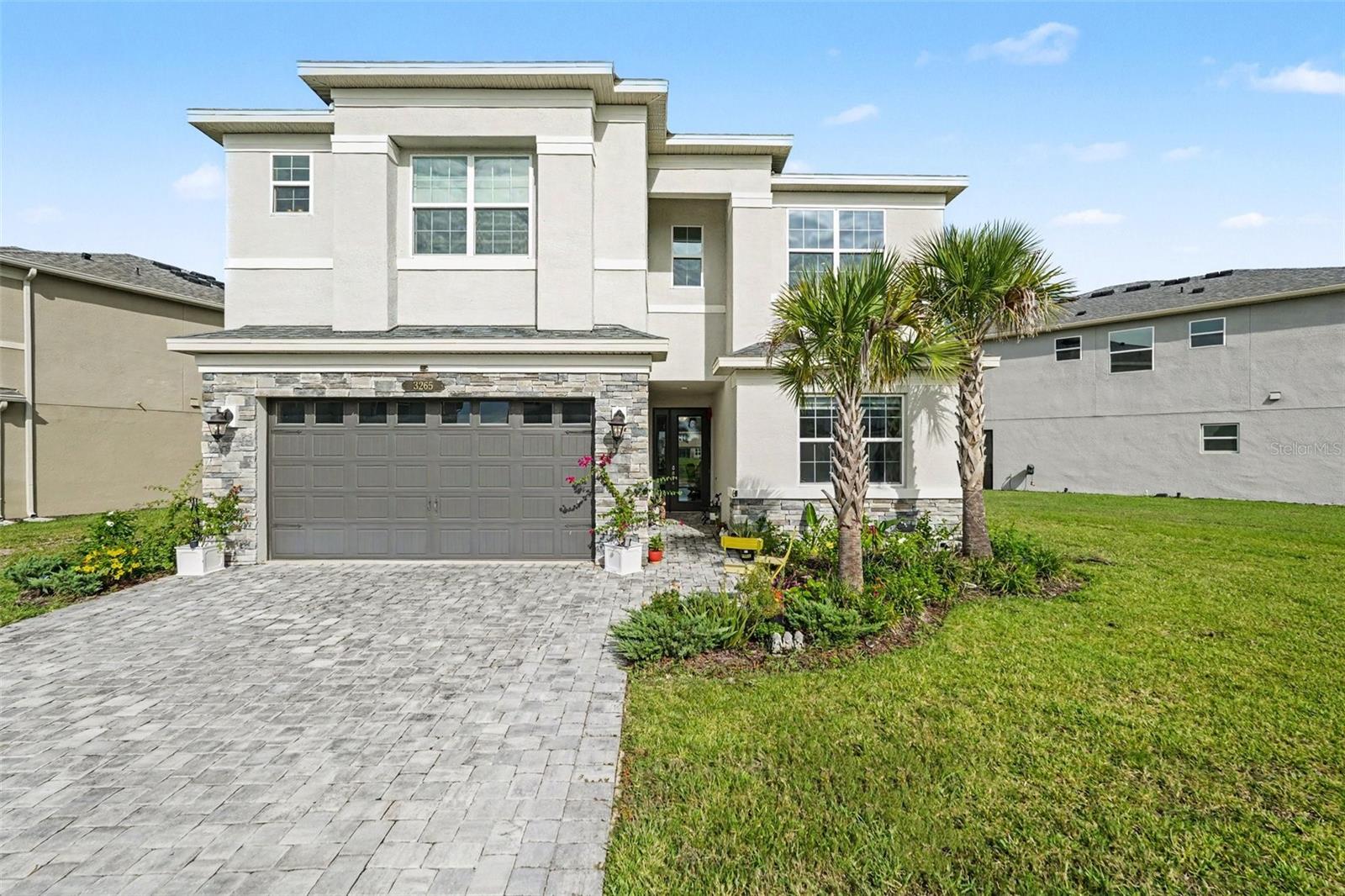 Two-story home with a stone-trimmed garage, paver driveway, and palm trees.