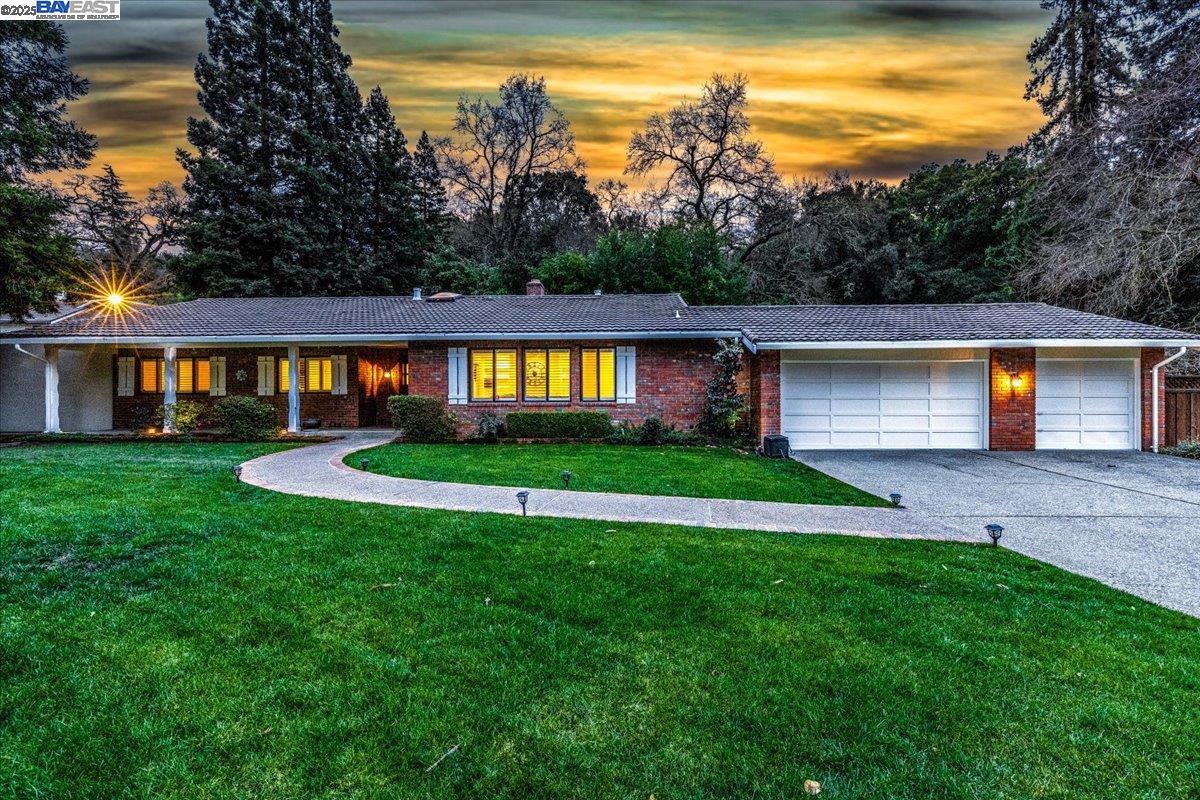 Single-story brick home at dusk with illuminated windows, a curved walkway, and a two-car garage.