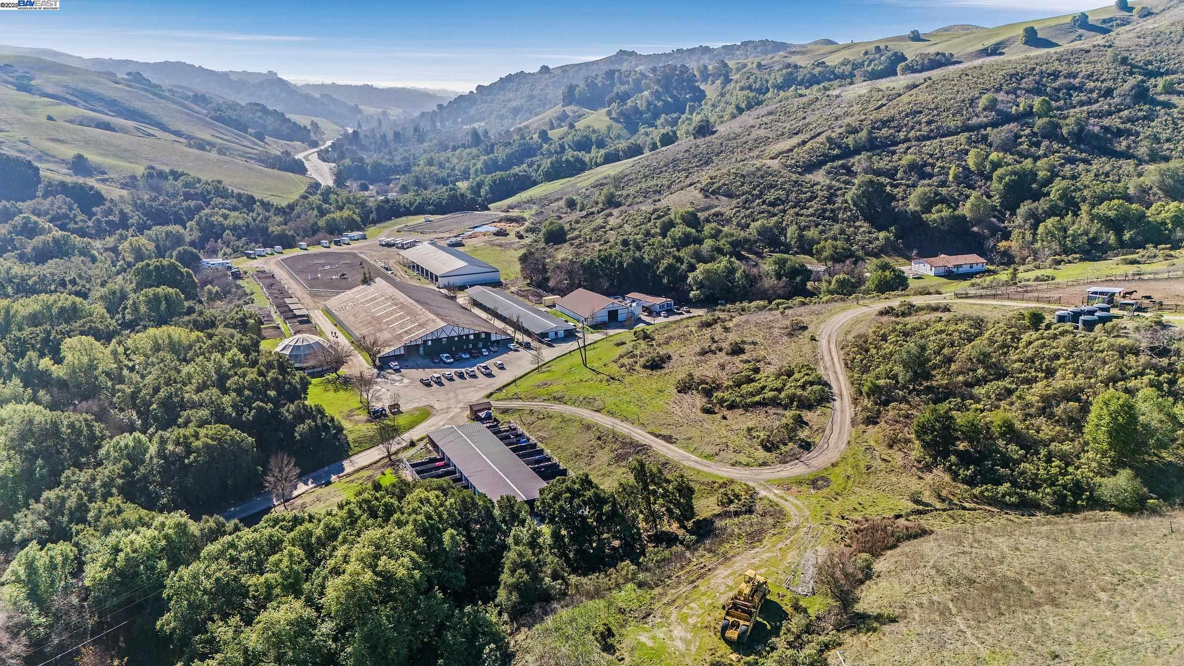 Rural equestrian property with a riding arena, barns, paddocks, and wooded hills.